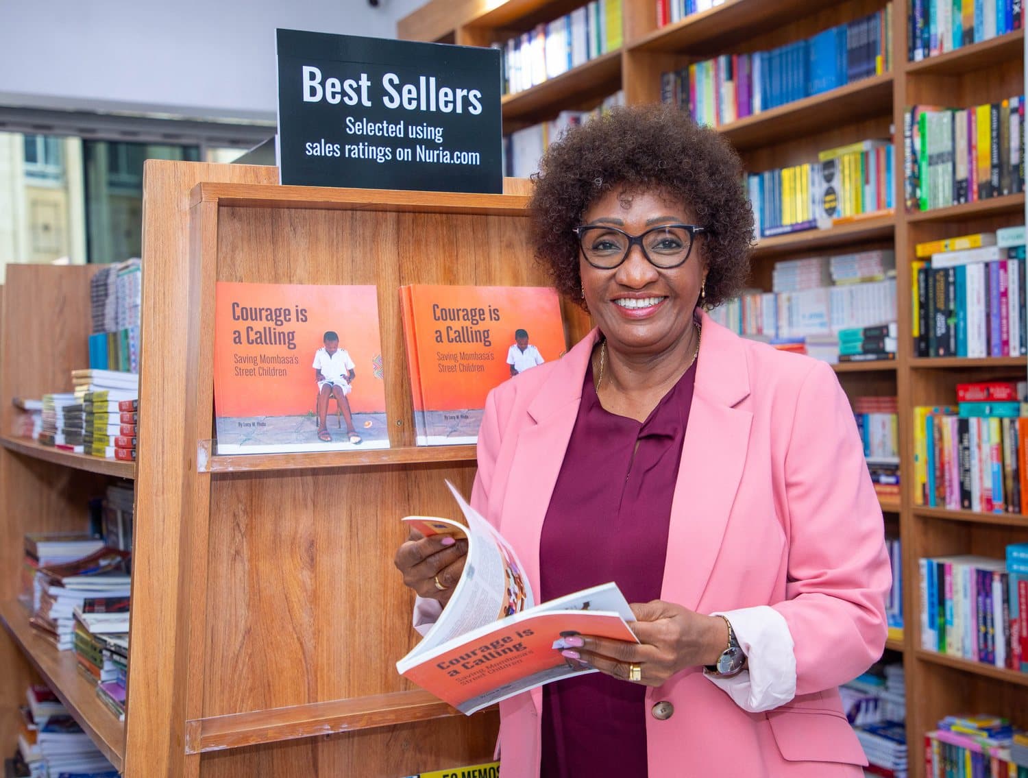 Lucy Yinda holding Courage is a Calling beside the bestsellers shelf at Nuria Bookstore