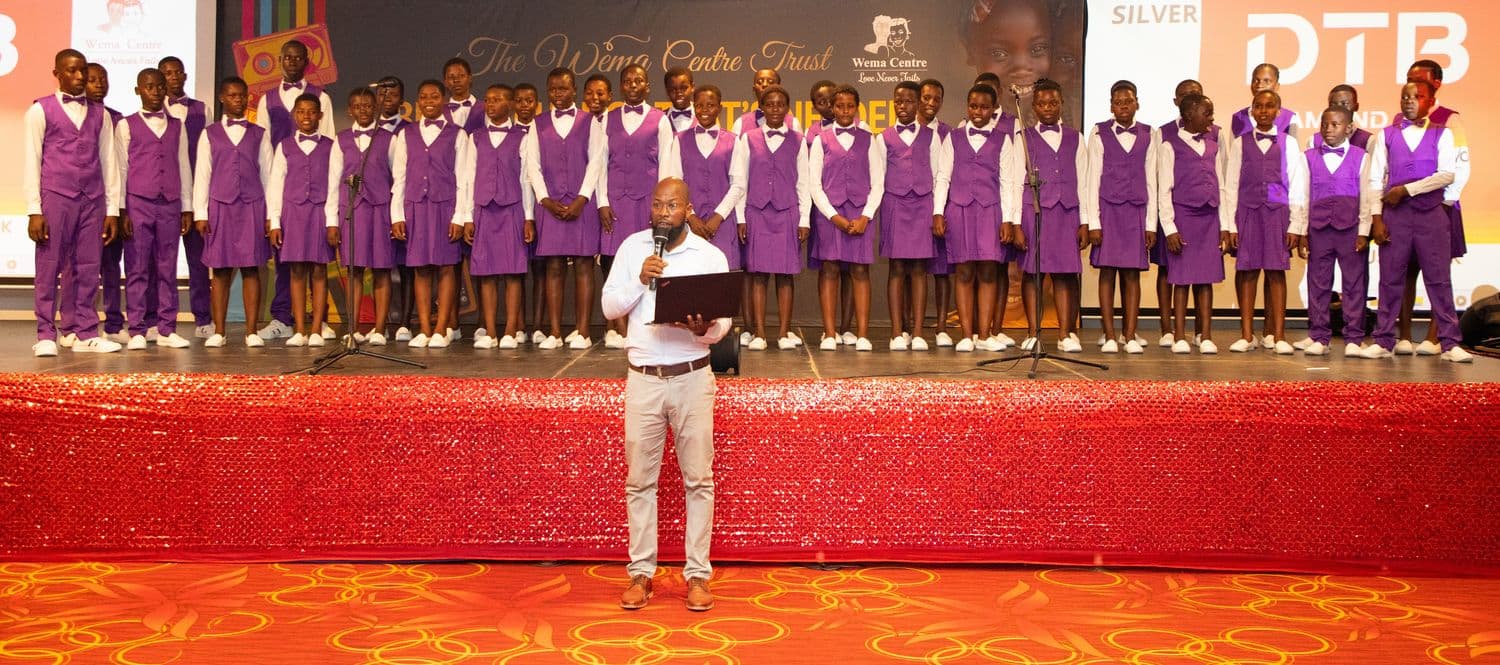 The Wema Centre Trust choir lined up on stage with a host addressing the audience
